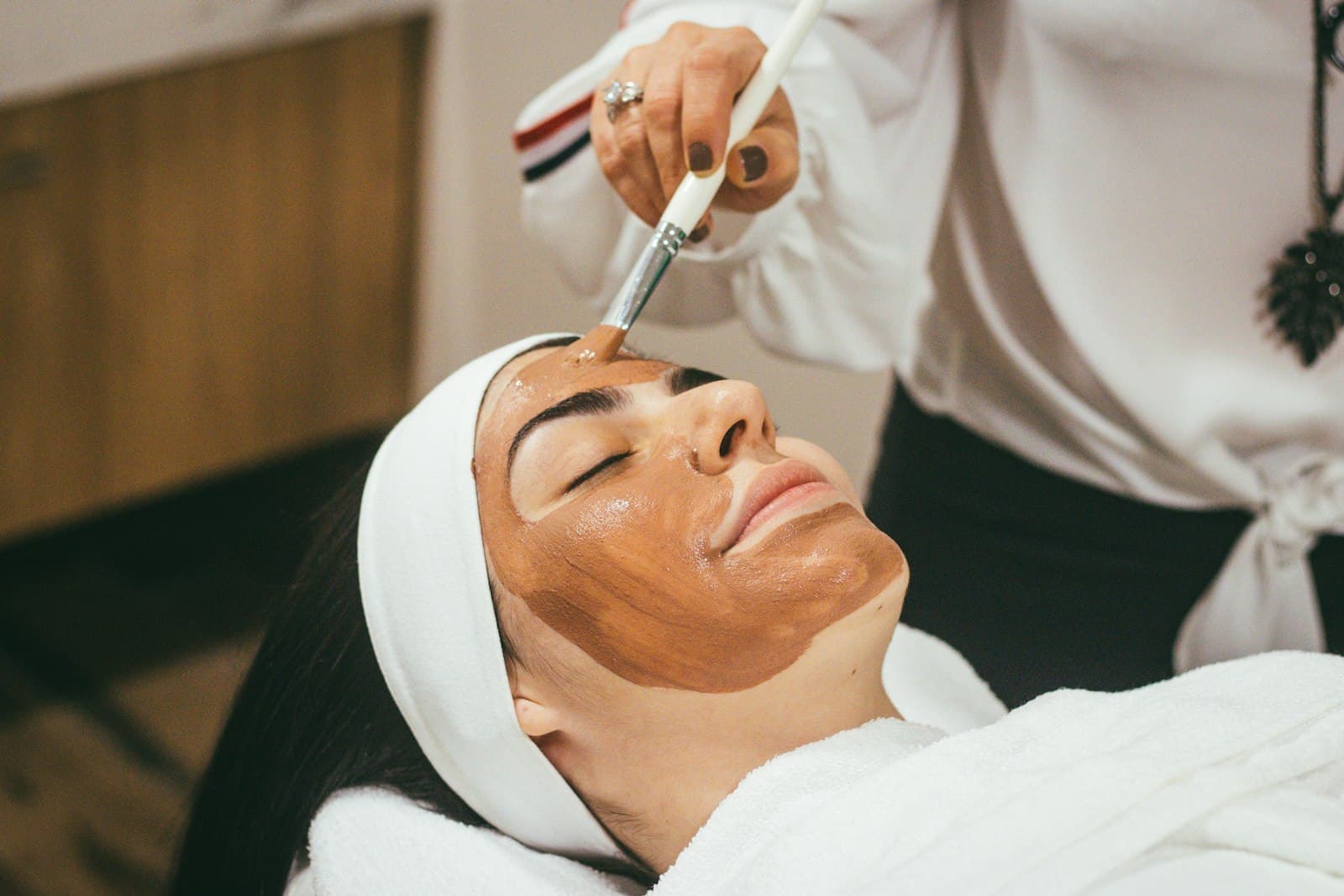 Esthetician applying a customized masque during a facial treatment.